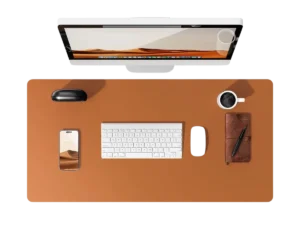 Vue de dessus d'un bureau organisé avec un tapis de souris cuir marron, un écran, un clavier et une tasse de café