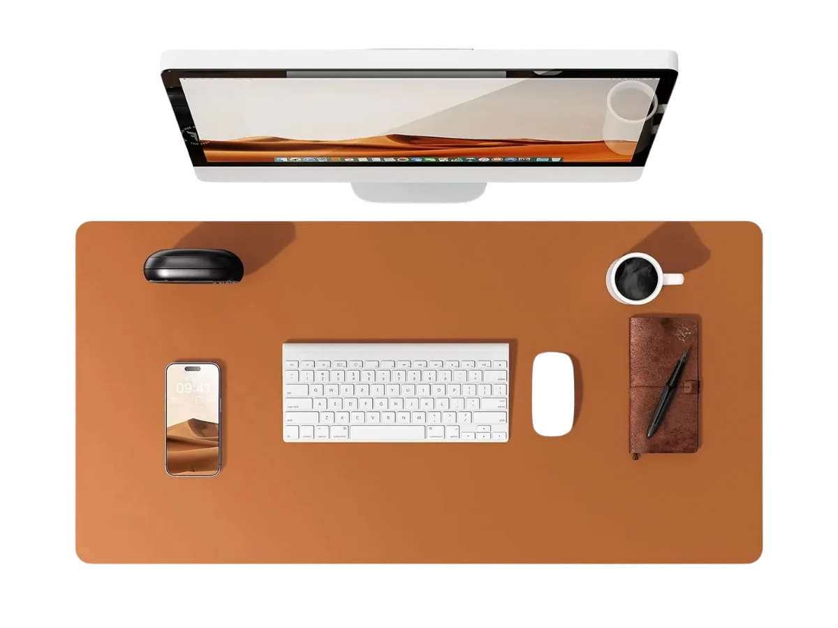 Vue de dessus d'un bureau organisé avec un tapis de souris cuir marron, un écran, un clavier et une tasse de café