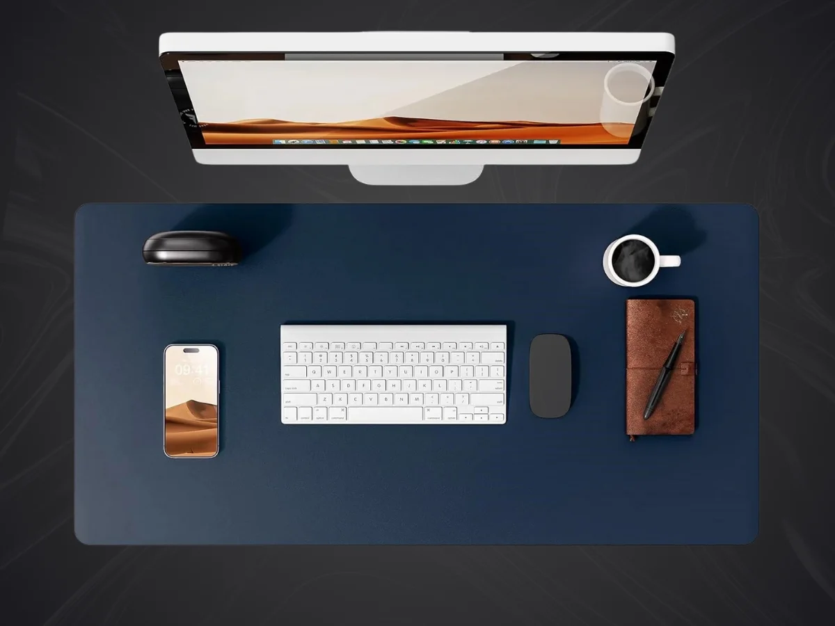 Vue de dessus d'un bureau moderne avec un grand tapis de souris simili cuir bleu, un écran d'ordinateur, clavier, souris et accessoires.