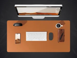 Vue de dessus d'un bureau avec un grand tapis de souris simili cuir marron-orangé, une tasse de café, un clavier, une souris et un smartphone.