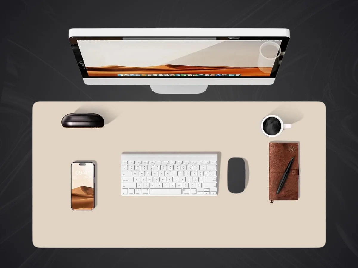 Vue de dessus d'un bureau organisé avec un grand tapis de souris simili cuir beige, clavier blanc, souris noire, smartphone, tasse de café et carnet.
