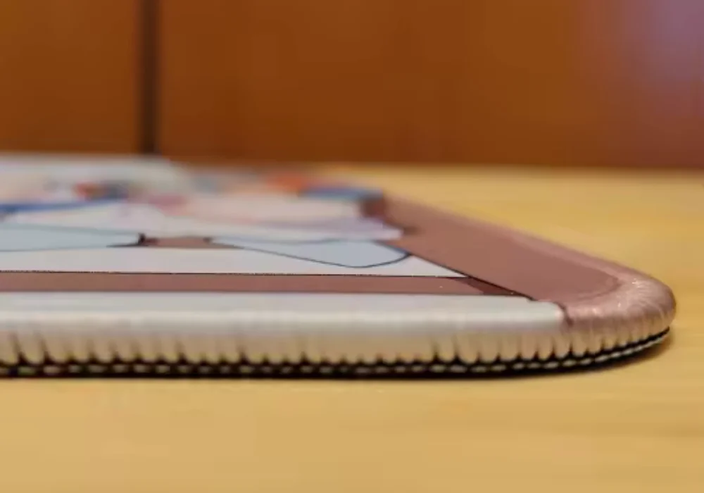 Gros plan sur le bord latéral d'un tapis de souris avec une illustration de style anime, présentant des coutures robustes.