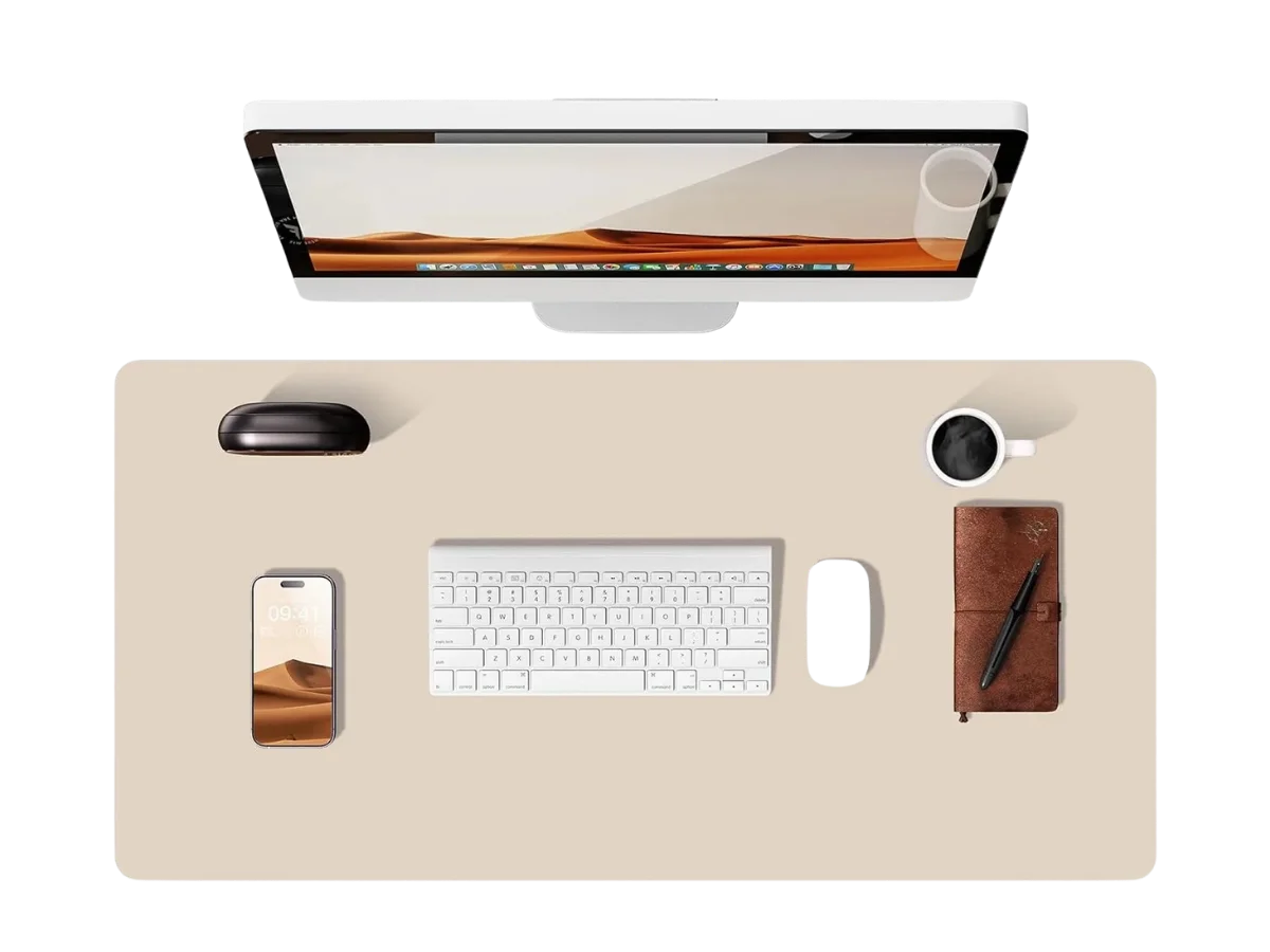 Vue de dessus d'un bureau avec un élégant tapis de souris cuir beige clair au centre, un clavier, une souris noire, un smartphone, un carnet marron, un stylo et une tasse de café sur la droite. Un moniteur est positionné en haut.